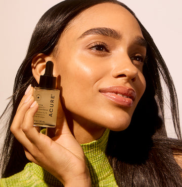 Woman with glowy and hydrated skin holding a glass jar of Brightening Vitamin C & Ferulic Acid next to her face